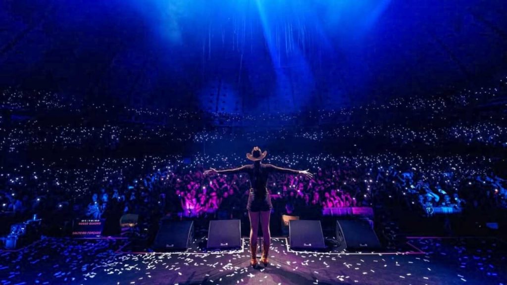 Foto da cantora Ana Castela no palco agradecendo ao público.